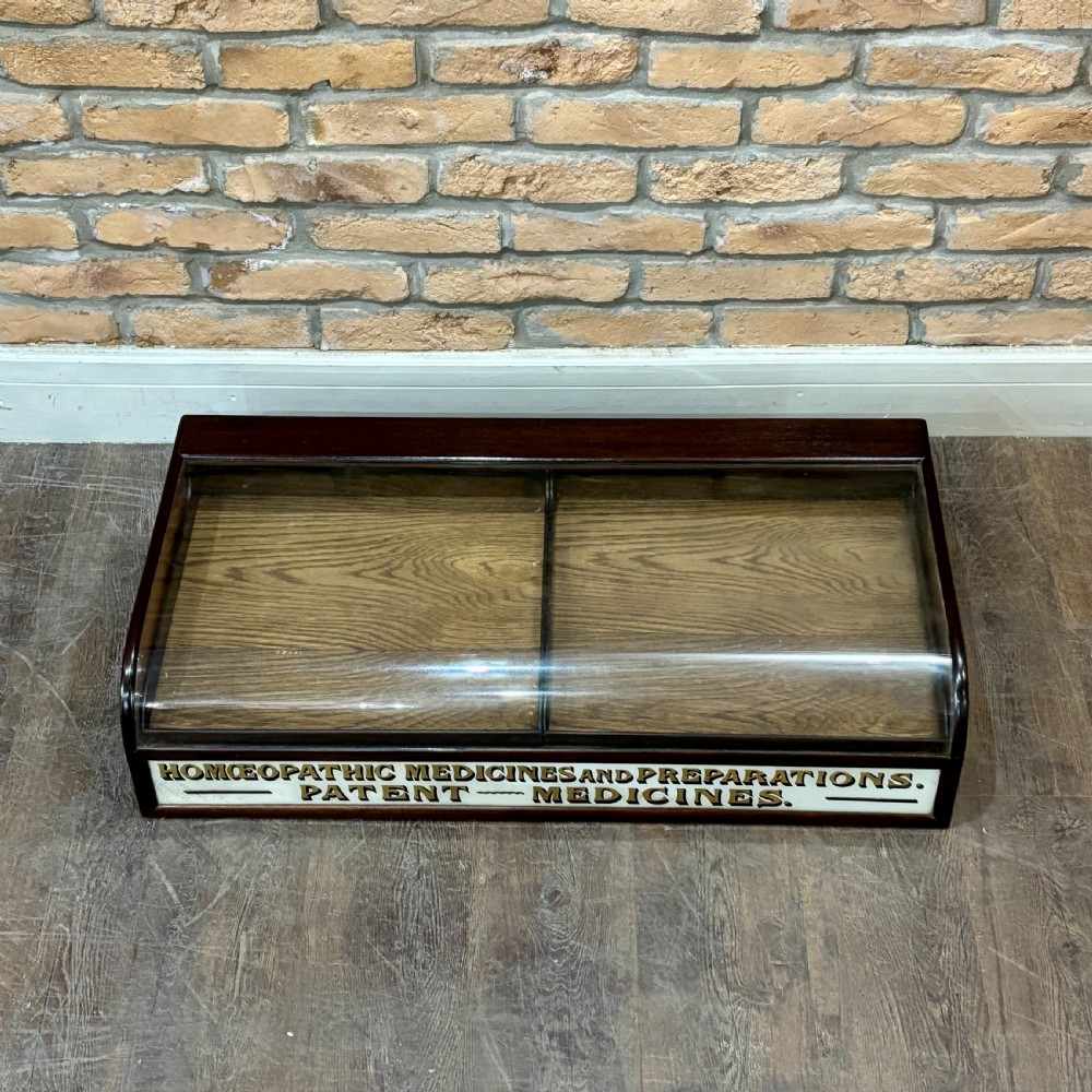 A Victorian mahogany countertop display cabinet featuring a curved glass front and a lower white panel reading Homoeopathic Medicines and Preparations. View II