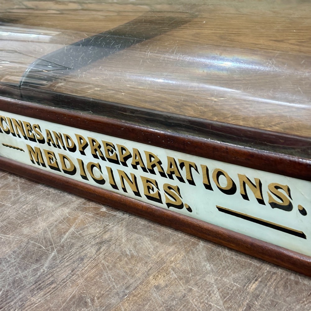 A Victorian mahogany countertop display cabinet featuring a curved glass front and a lower white panel reading Homoeopathic Medicines and Preparations. View III