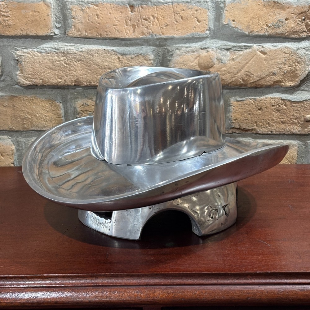 A cast aluminium milliners hat block mould in the shape of a wide-brimmed hat sitting on a polished dark wood surface.
