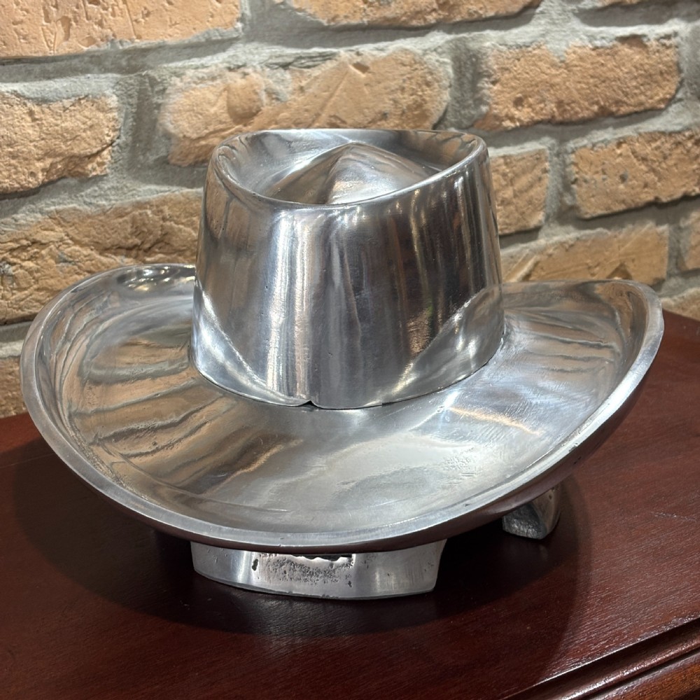 A cast aluminium milliners hat block mould in the shape of a wide-brimmed hat sitting on a polished dark wood surface. View II