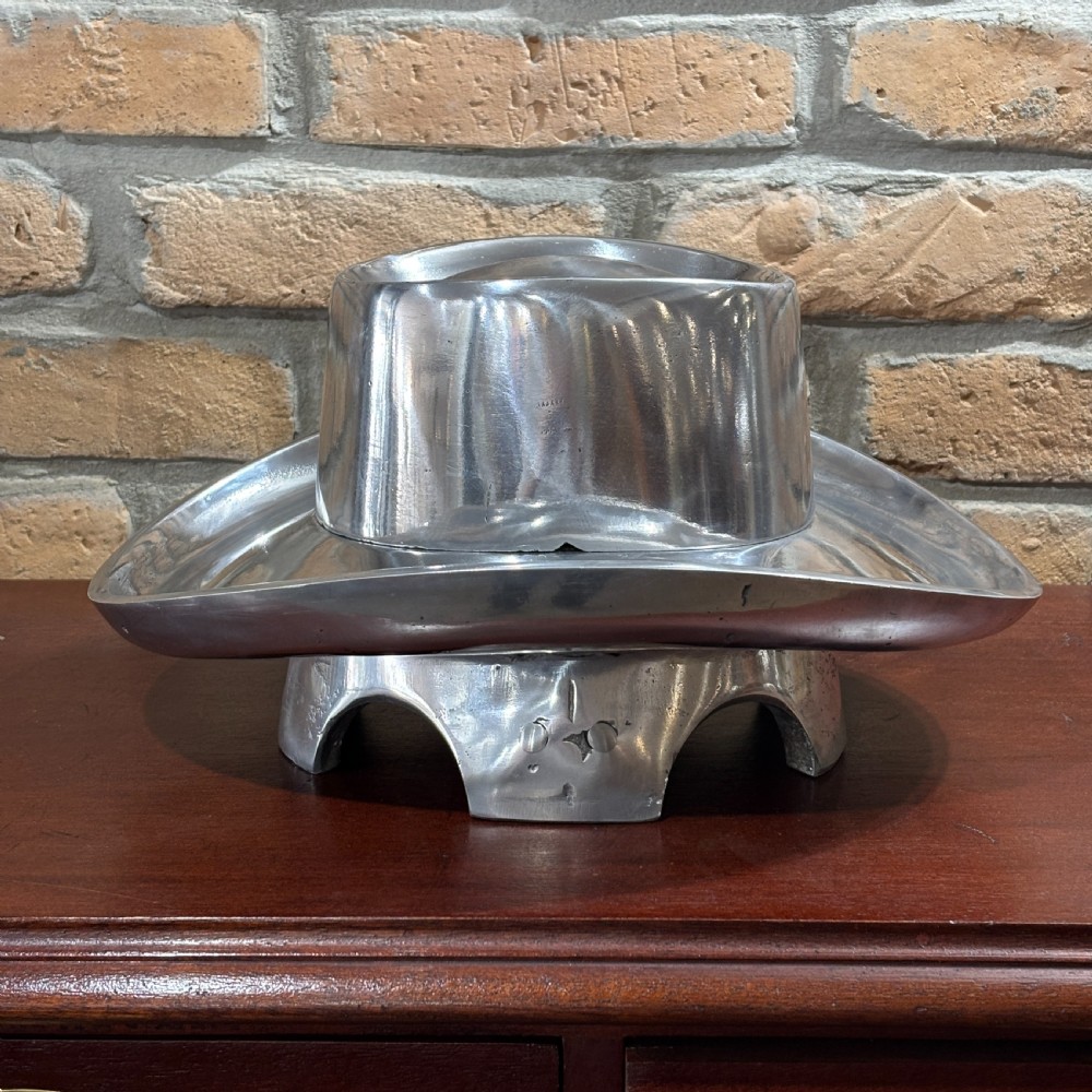 A cast aluminium milliners hat block mould in the shape of a wide-brimmed hat sitting on a polished dark wood surface. View IV