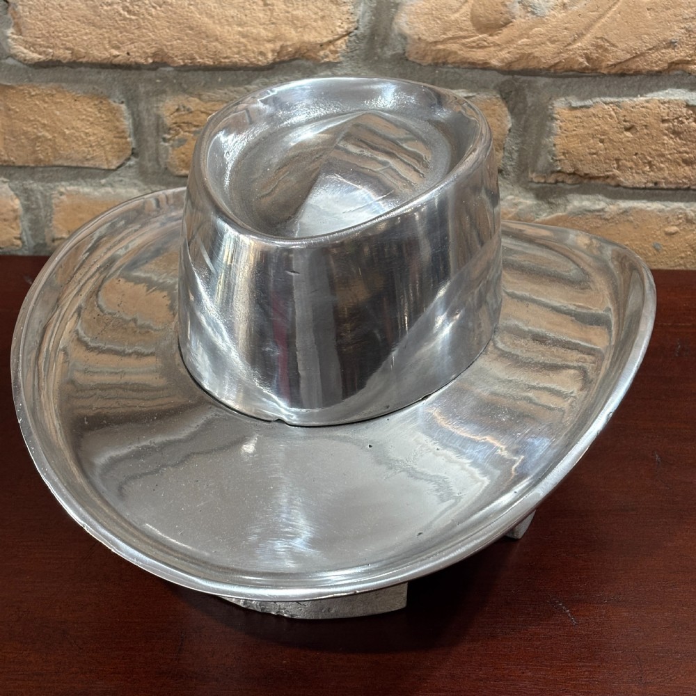 A cast aluminium milliners hat block mould shaped like a broad-brimmed cowboy hat with a polished silver metallic finish. View II