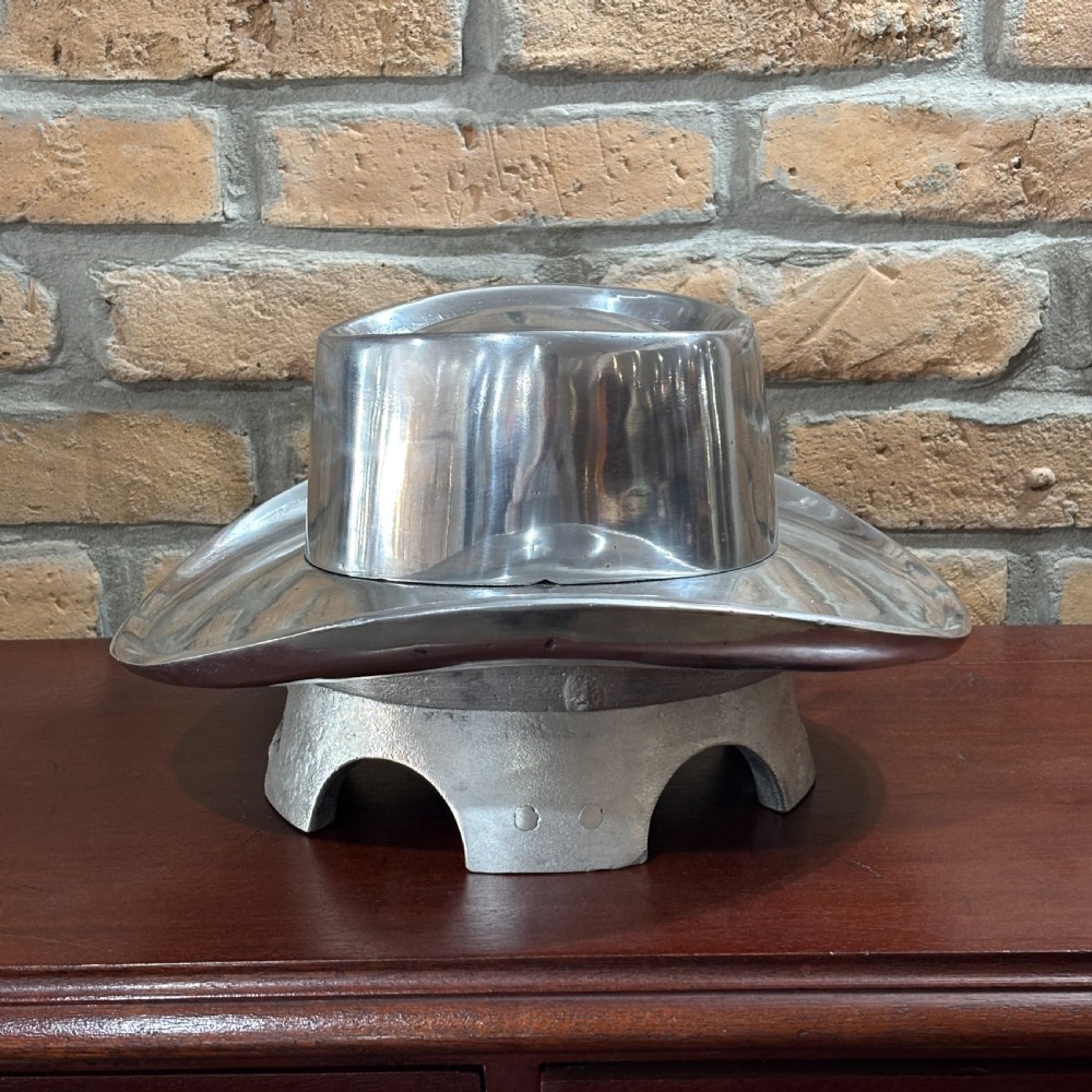 A cast aluminium milliners hat block mould shaped like a broad-brimmed cowboy hat with a polished silver metallic finish. View III