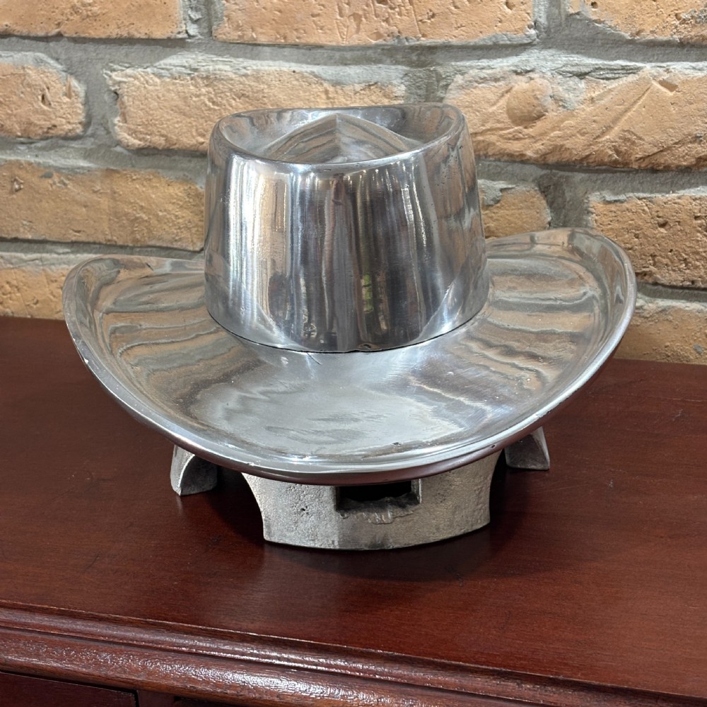 A cast aluminium milliners hat block mould shaped like a broad-brimmed cowboy hat with a polished silver metallic finish. View IV