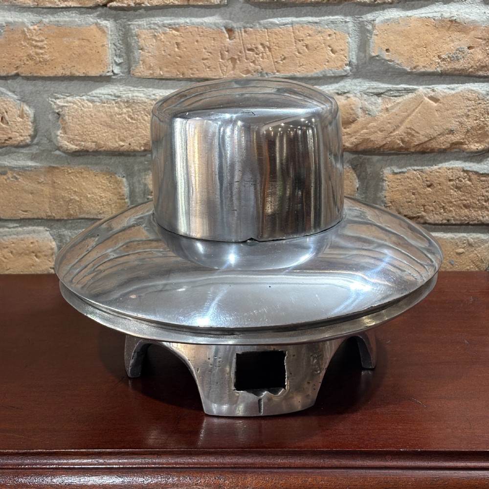 A polished silver cast aluminium milliners hat mould featuring a rounded crown section and flared brim contour resting on a hollow base. View II