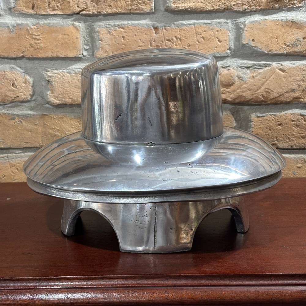 A polished silver cast aluminium milliners hat mould featuring a rounded crown section and flared brim contour resting on a hollow base. View IV