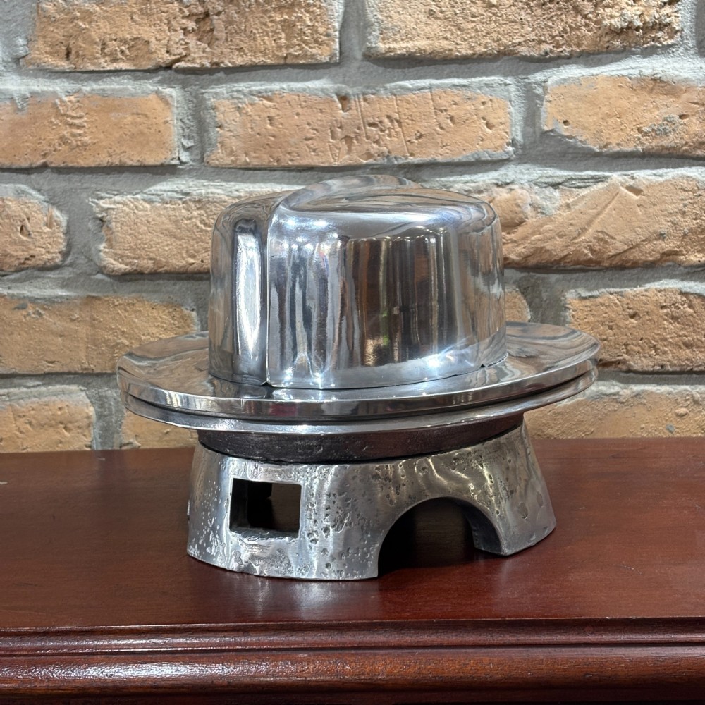 A polished cast aluminium millinery hat block mould forming a fedora shape on a contoured pedestal base. View II