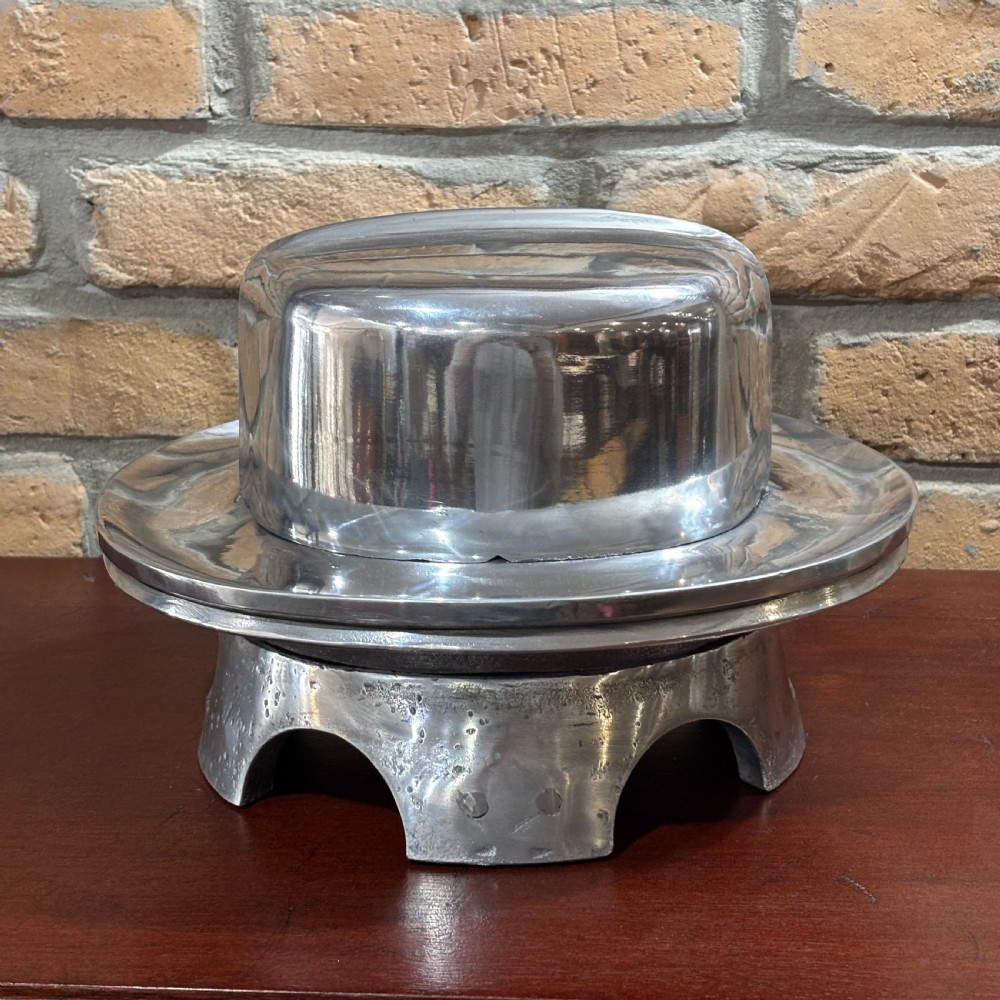A polished cast aluminium millinery hat block mould forming a fedora shape on a contoured pedestal base. View III