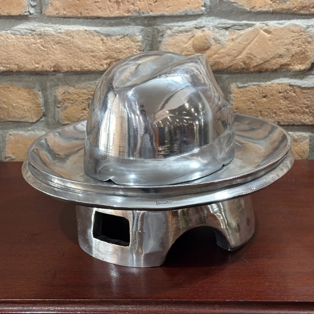 A polished cast aluminium milliners hat block mould featuring a fedora crown and wide brim mounted on a hollow metallic base.