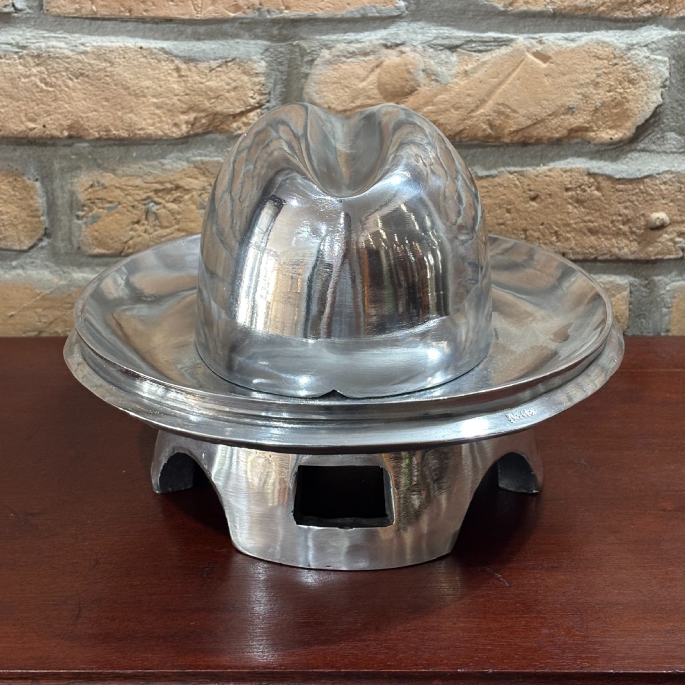 A polished cast aluminium milliners hat block mould featuring a fedora crown and wide brim mounted on a hollow metallic base. View II