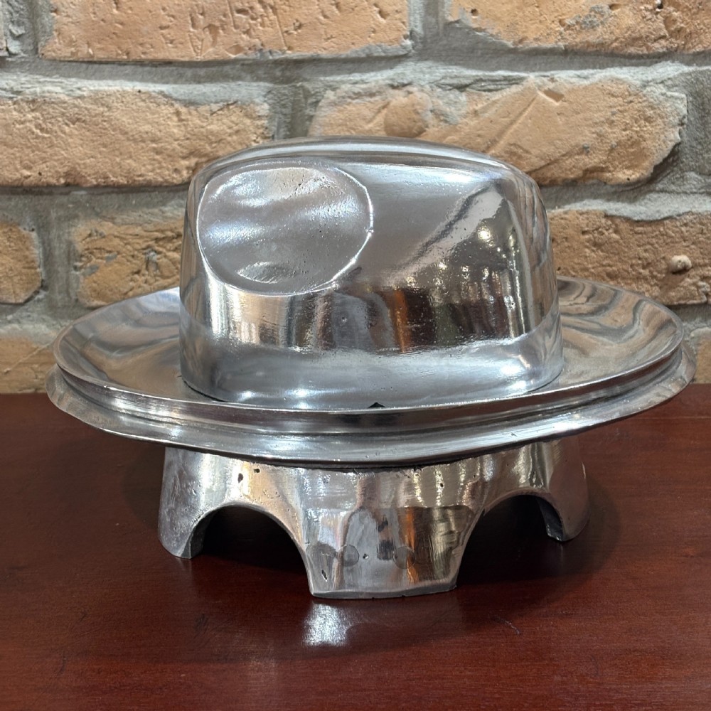 A polished cast aluminium milliners hat block mould featuring a fedora crown and wide brim mounted on a hollow metallic base. View III