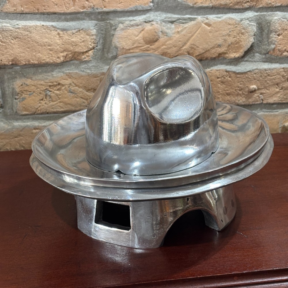 A polished cast aluminium milliners hat block mould featuring a fedora crown and wide brim mounted on a hollow metallic base. View IV