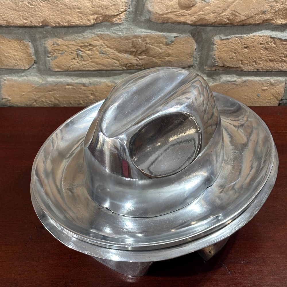 A polished cast aluminium milliners hat block mould featuring a fedora crown and wide brim mounted on a hollow metallic base. View V