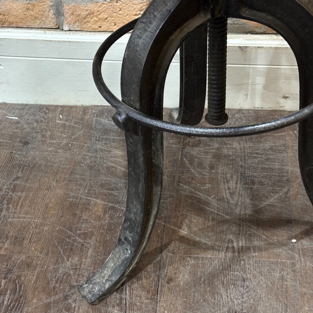 An adjustable industrial workshop stool featuring a circular dark wood seat supported by a black cast iron tripod base with a central screw mechanism and circular footrest. View III