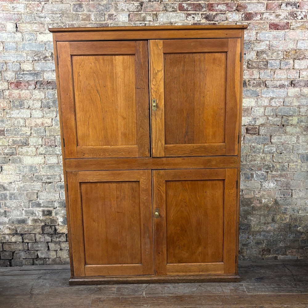 A full-frontal shot of a tall wooden 1930s general store cabinet featuring four panelled doors and brass hardware.