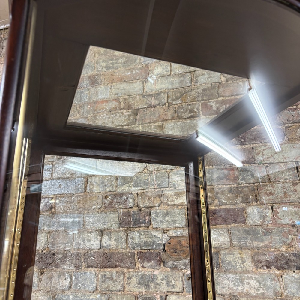 A tall freestanding Edwardian mahogany shop display cabinet with curved glass front, glass side panels, and brass adjustable shelf supports. View II