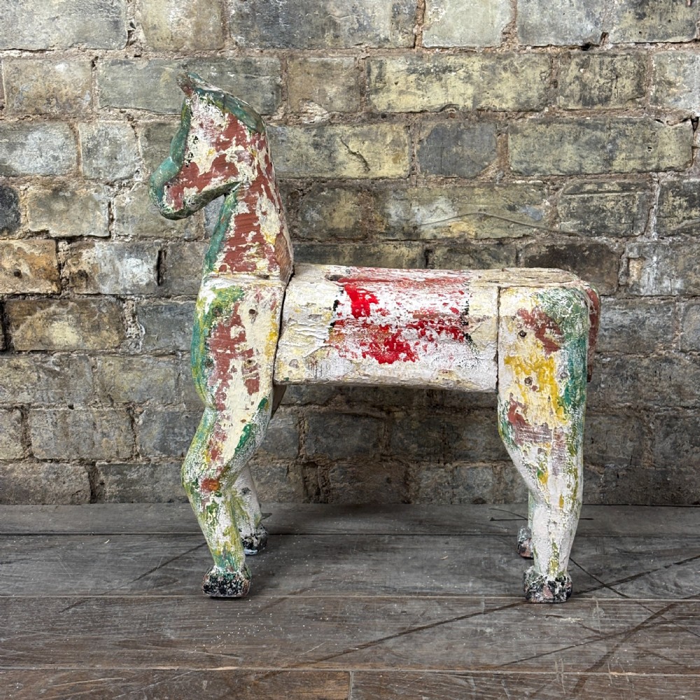 A carved wooden toy horse displaying a heavily distressed polychrome painted finish in layers of white, red, green, and yellow.