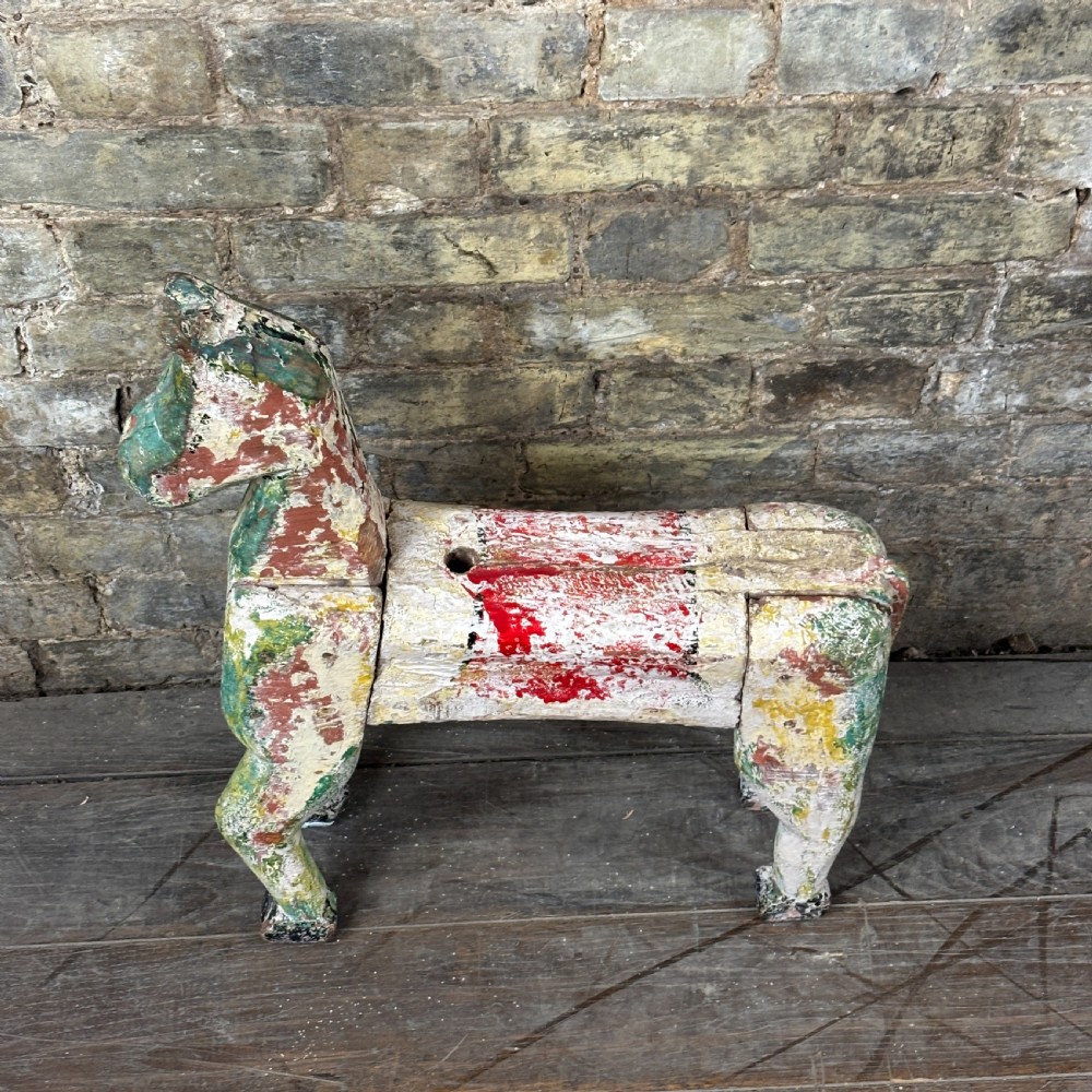 A carved wooden toy horse displaying a heavily distressed polychrome painted finish in layers of white, red, green, and yellow. View II