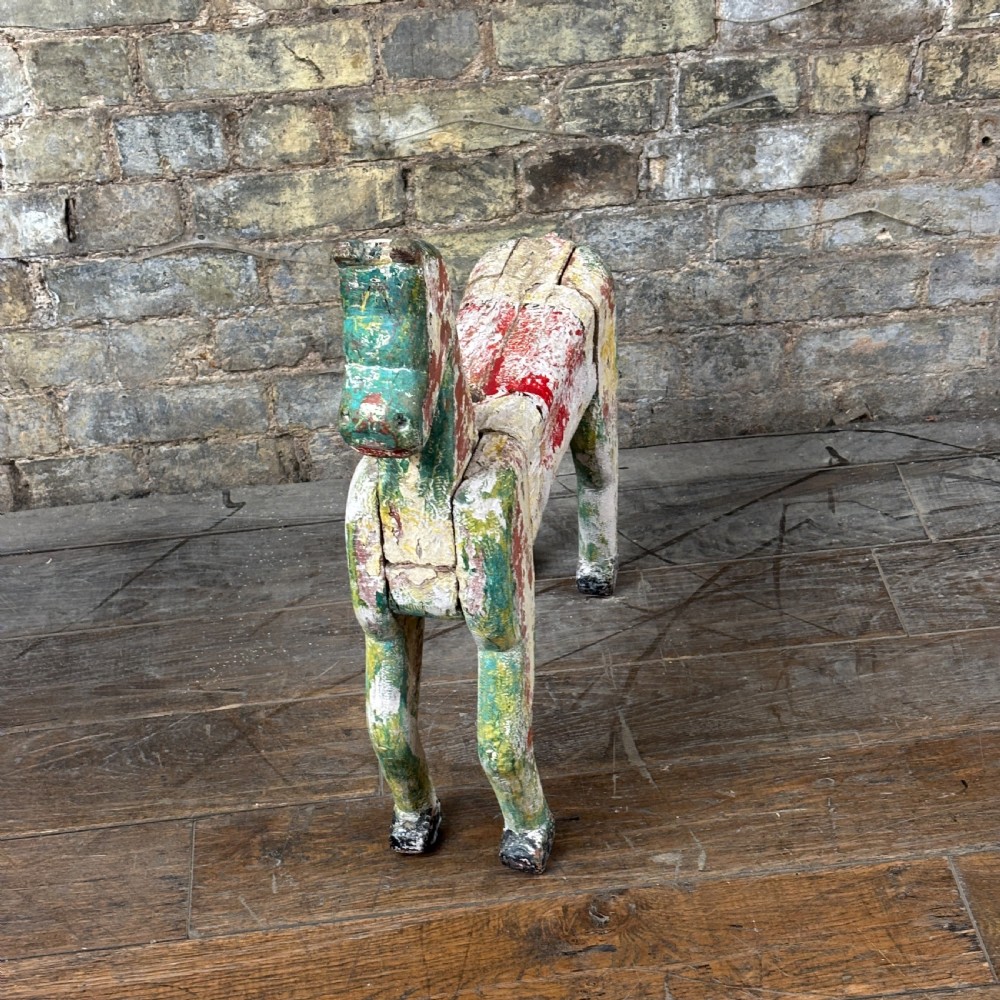 A carved wooden toy horse displaying a heavily distressed polychrome painted finish in layers of white, red, green, and yellow. View III
