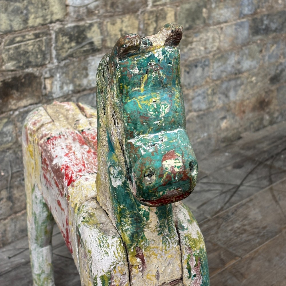 A carved wooden toy horse displaying a heavily distressed polychrome painted finish in layers of white, red, green, and yellow. View IV