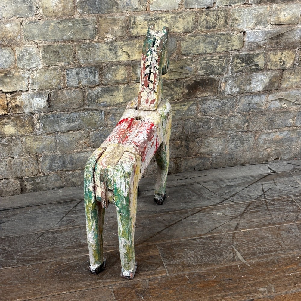A carved wooden toy horse displaying a heavily distressed polychrome painted finish in layers of white, red, green, and yellow. View V
