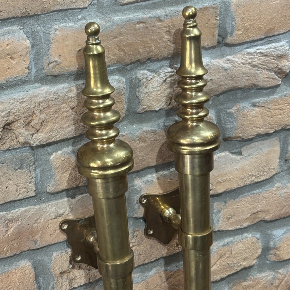A pair of long, vertical antique brass door pull handles featuring turned urn finials at the top and mounting brackets. View V