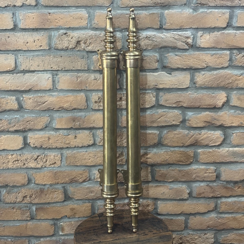 A pair of long tubular brass shop door handles featuring turned finials on each end and side mounting brackets.