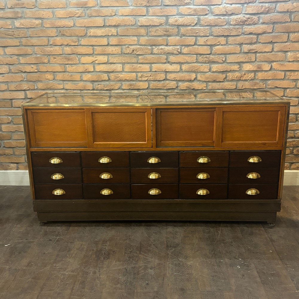 A 1930s brass-framed shop display counter featuring glass side and top panels, tiered interior timber display bins, and timber sliding back doors. View II