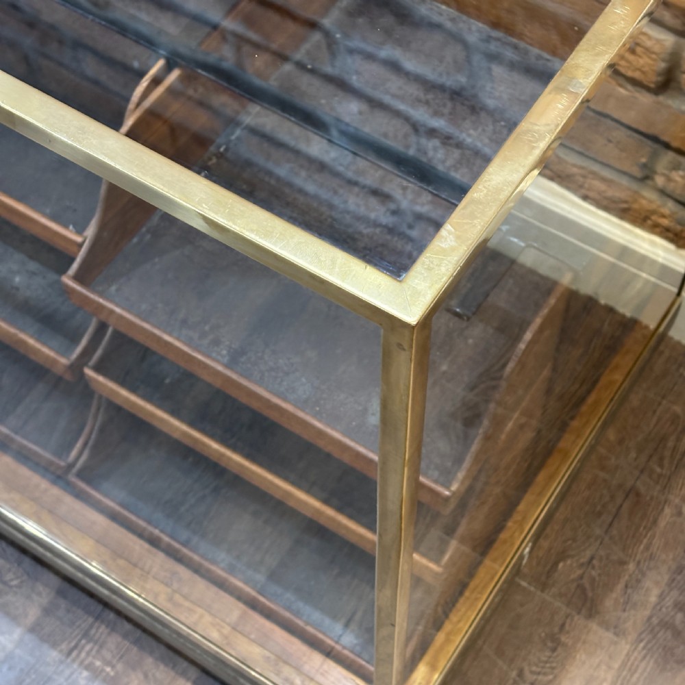 A 1930s brass-framed shop display counter featuring glass side and top panels, tiered interior timber display bins, and timber sliding back doors. View V