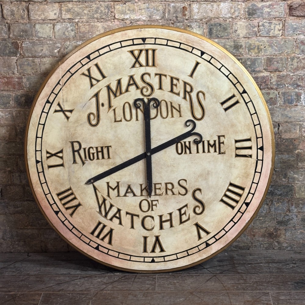 A large circular painted clock face featuring Roman numerals and hand-lettered text reading J Masters London, Right On Time, Makers of Watches.