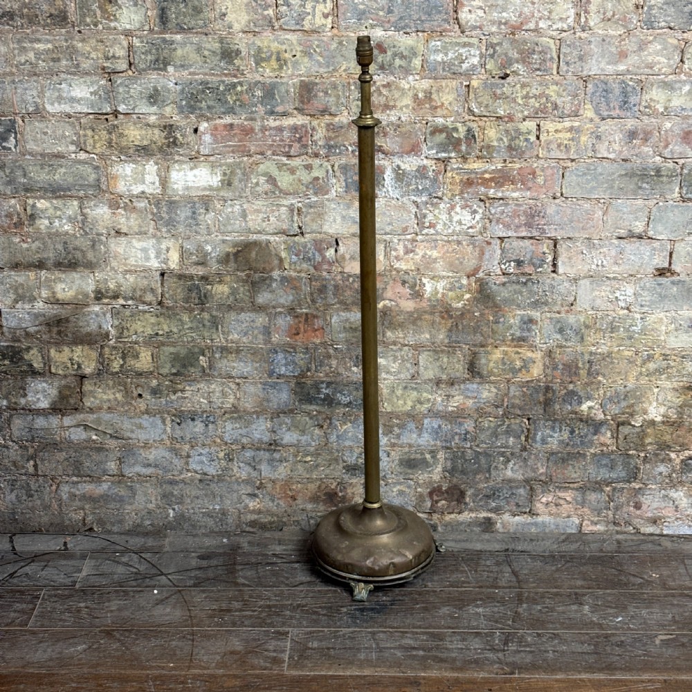 An antique Edwardian turned brass floor lamp stand featuring a weighted domed base on small feet and a slender central column.