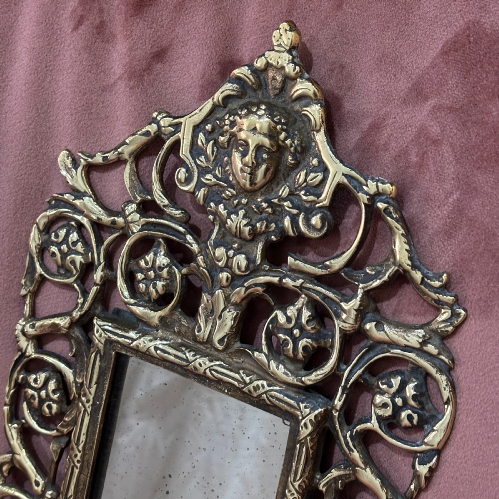 A rectangular glass mirror set within an ornate cast brass frame featuring pierced scrollwork and a central mask crest at the top. View II