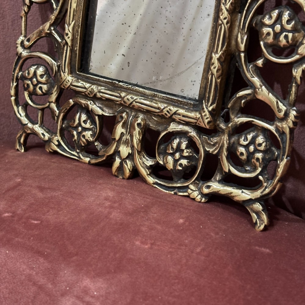 A rectangular glass mirror set within an ornate cast brass frame featuring pierced scrollwork and a central mask crest at the top. View III