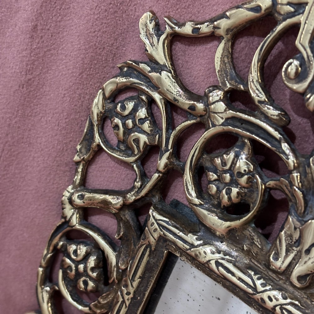 A rectangular glass mirror set within an ornate cast brass frame featuring pierced scrollwork and a central mask crest at the top. View IV