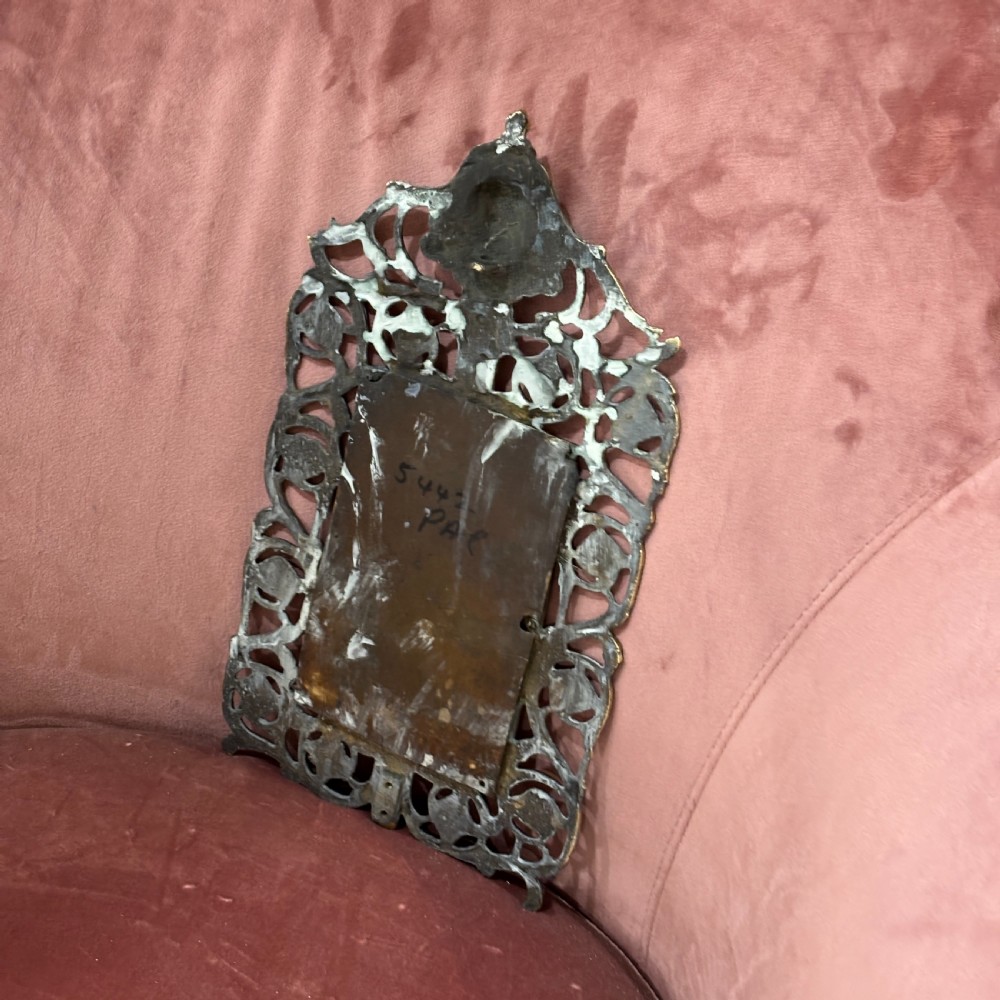 A rectangular glass mirror set within an ornate cast brass frame featuring pierced scrollwork and a central mask crest at the top. View V
