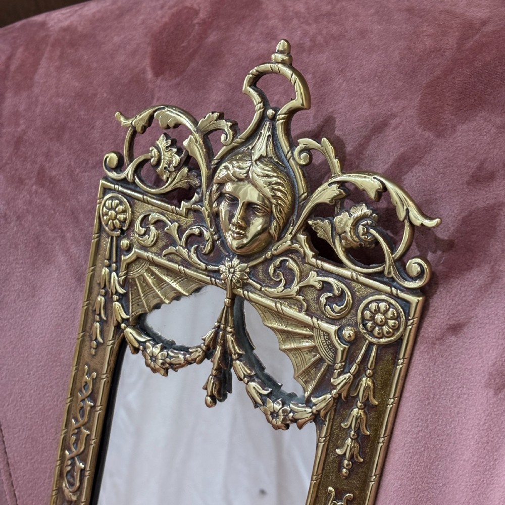 A pair of rectangular brass wall mirrors featuring ornate classical mask crestings, floral garlands, and scrolled detailing. View II
