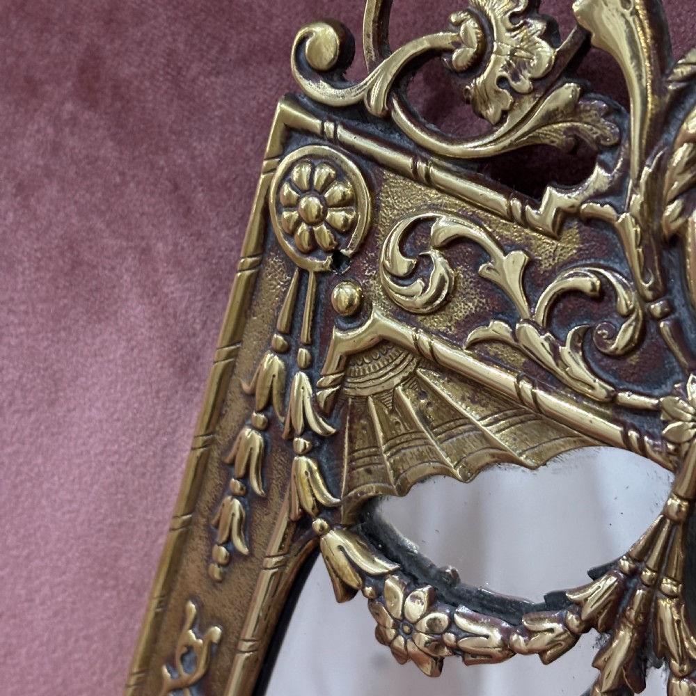 A pair of rectangular brass wall mirrors featuring ornate classical mask crestings, floral garlands, and scrolled detailing. View V