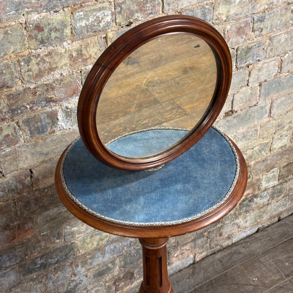 A Victorian mahogany shaving stand featuring a circular tilting mirror mounted above a blue fabric-lined shelf, supported by a turned column and tripod scroll legs. View II