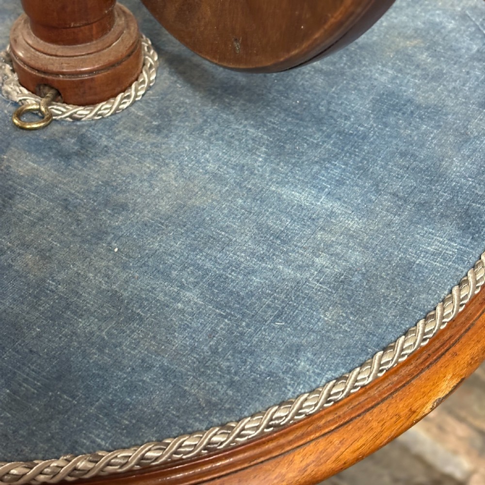 A Victorian mahogany shaving stand featuring a circular tilting mirror mounted above a blue fabric-lined shelf, supported by a turned column and tripod scroll legs. View V
