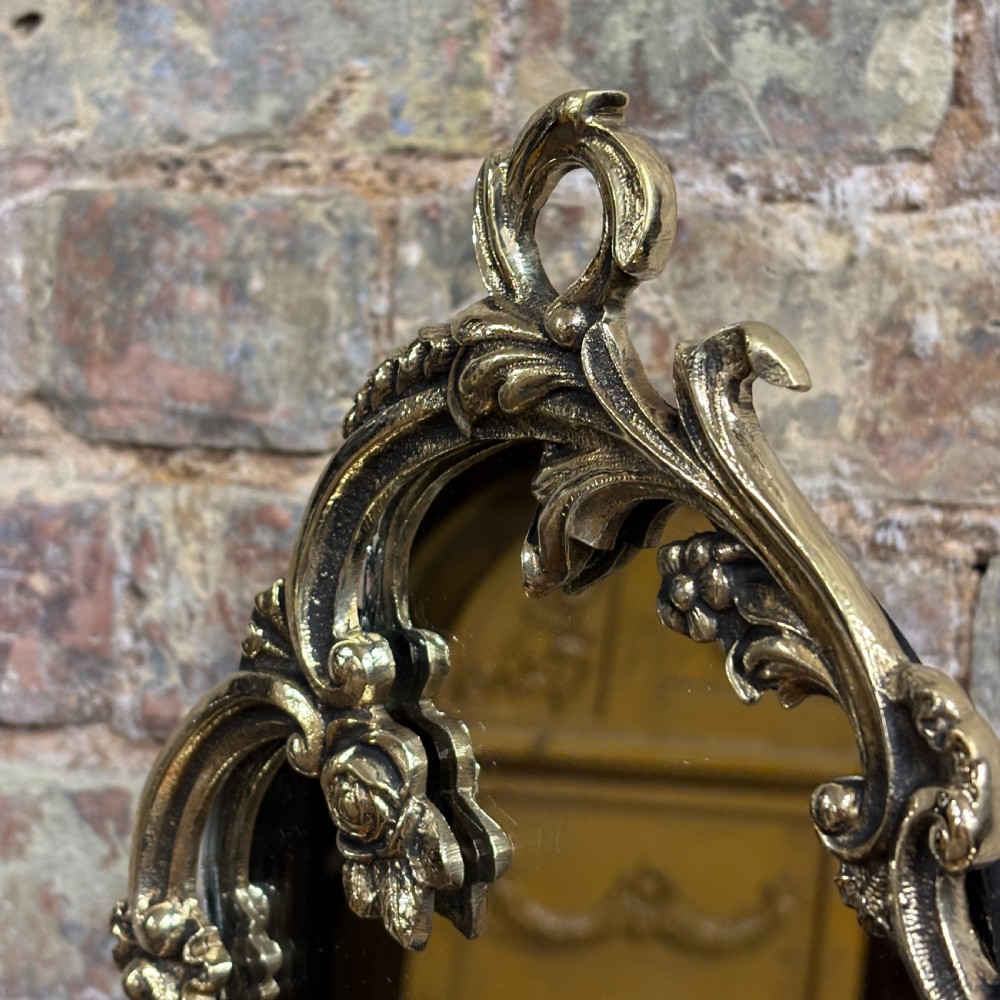 An ornate 1930s cast brass dressing table mirror with detailed floral scrollwork, an oval mirror frame, and a sturdy pedestal base. View V