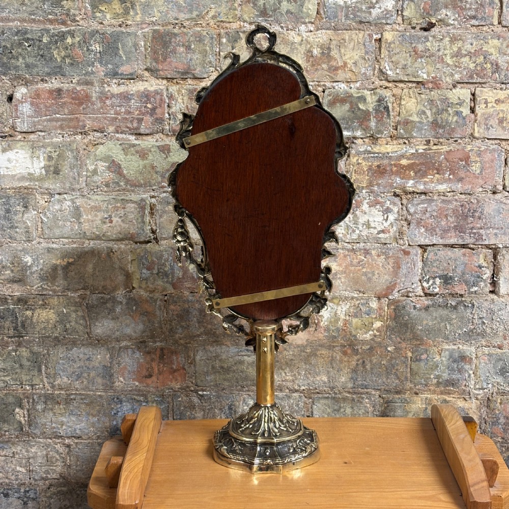 An ornate 1930s cast brass dressing table mirror with detailed floral scrollwork, an oval mirror frame, and a sturdy pedestal base. View VI