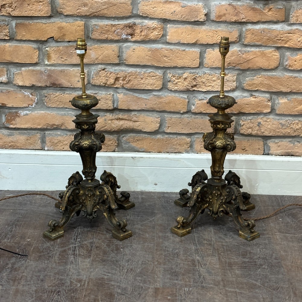 A pair of late Victorian gilt bronze lamp bases featuring ornate scrolling foliate designs, tripod feet, and raised brass light sockets.