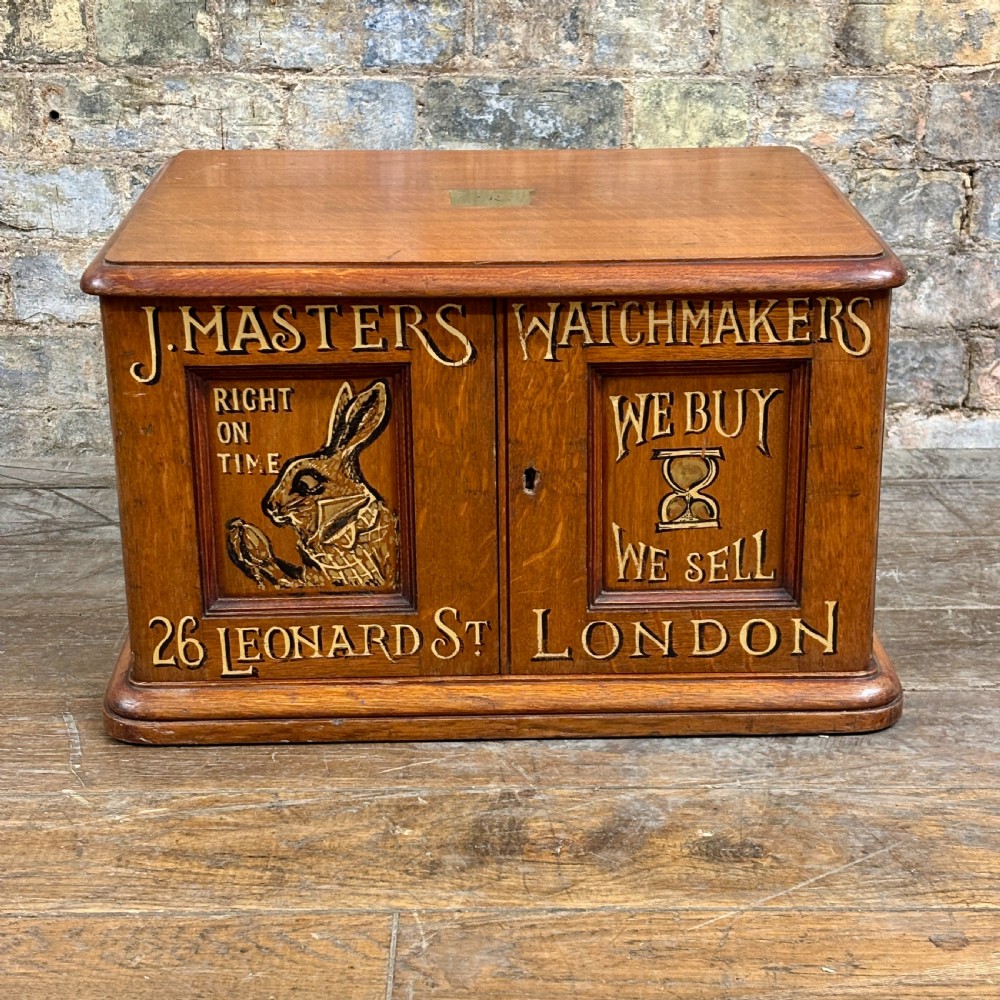 A small 1930s warm brown oak desktop cabinet with two panelled doors featuring hand-painted trade lettering and a rabbit illustration.