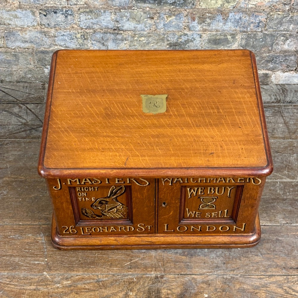 A small 1930s warm brown oak desktop cabinet with two panelled doors featuring hand-painted trade lettering and a rabbit illustration. View II