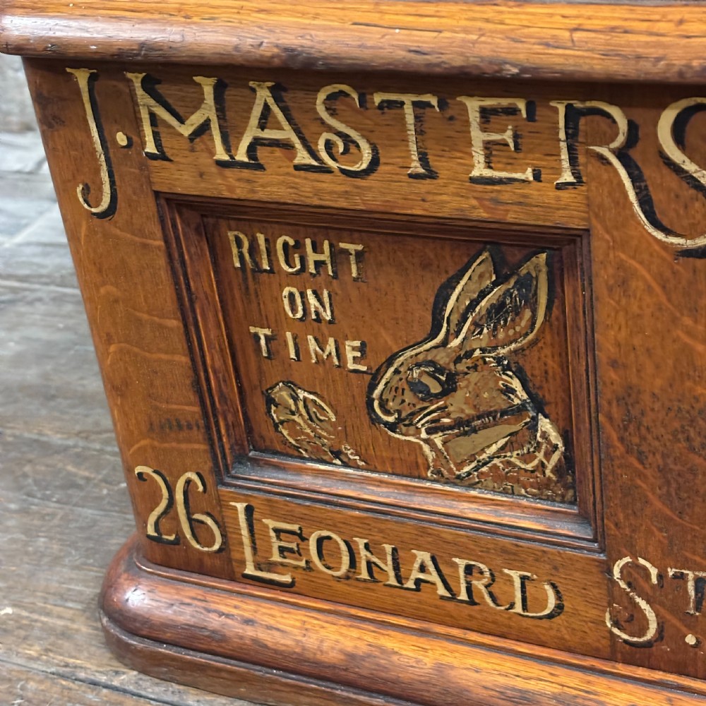 An antique carved oak tabletop cabinet featuring twin doors decorated with carved trade lettering and an illustration of a hare. View II