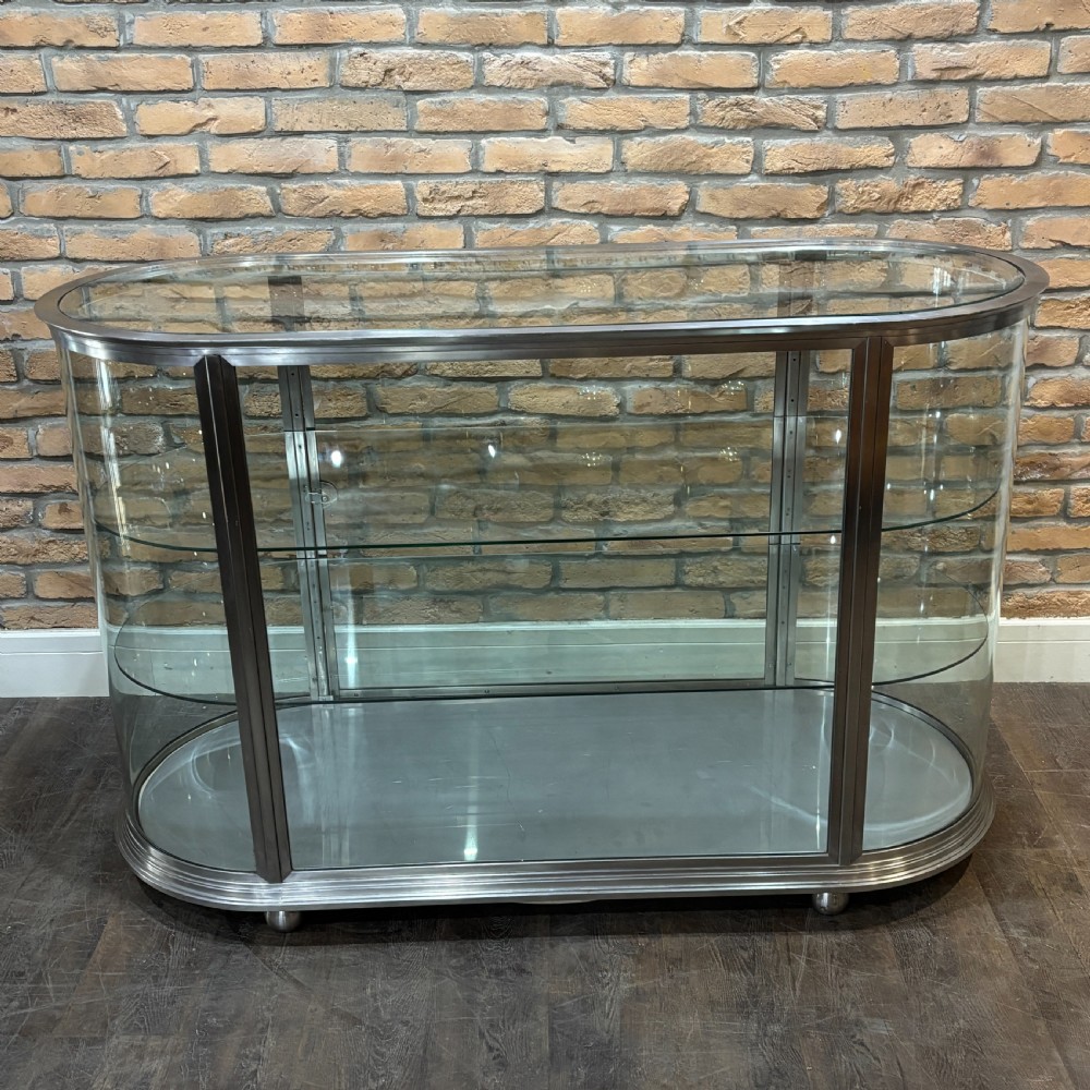 A 1930s Art Deco aluminium display counter with curved glass ends, internal glass shelves, and a metal base on small ball feet. View IV