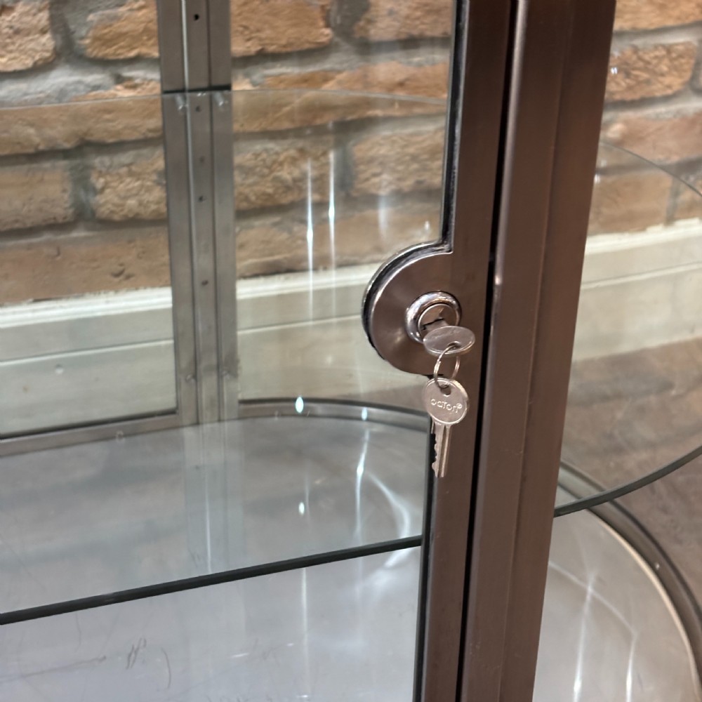 A 1930s Art Deco aluminium display counter with curved glass ends, internal glass shelves, and a metal base on small ball feet. View V