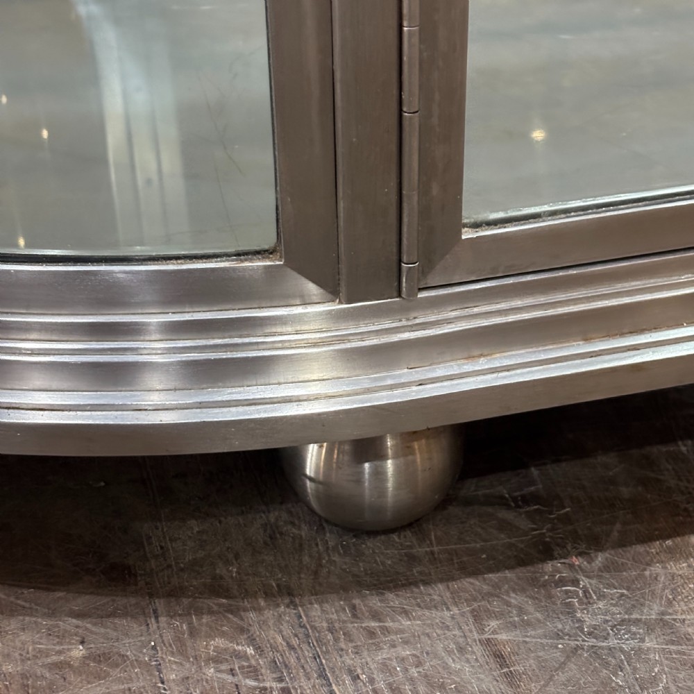 A 1930s Art Deco aluminium display counter with curved glass ends, internal glass shelves, and a metal base on small ball feet. View VI