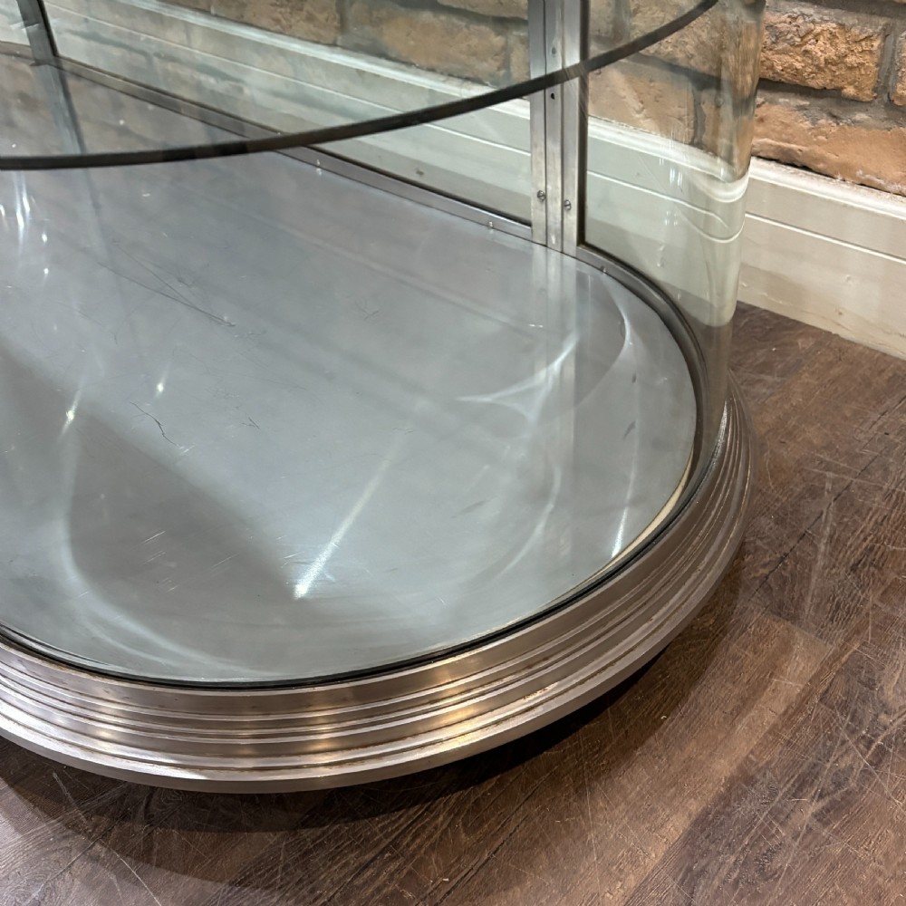 A 1930s Art Deco aluminium display counter with curved glass ends, internal glass shelves, and a metal base on small ball feet. View VII
