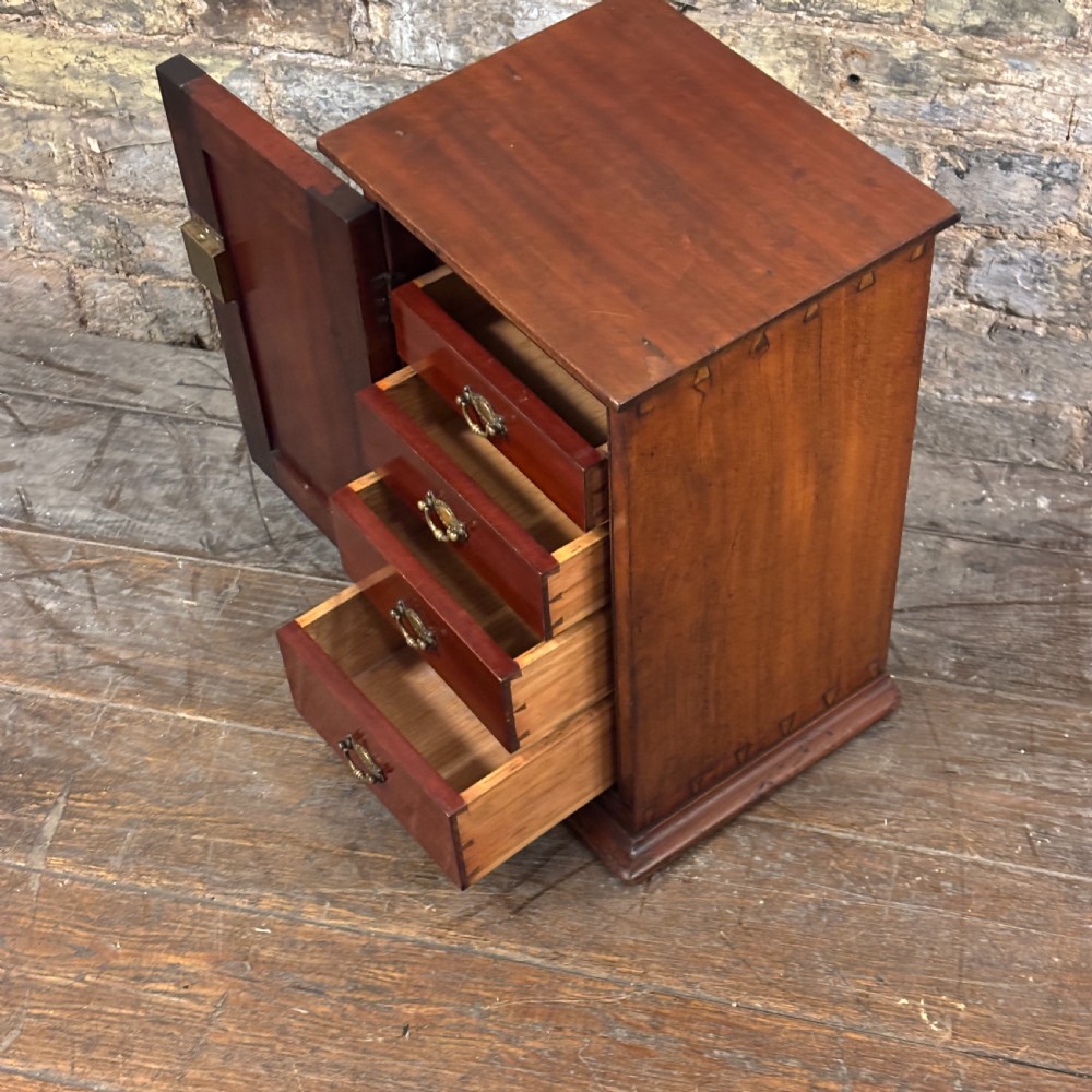 A compact dark mahogany tabletop cabinet featuring a single recessed panel door with a keyhole, a slanted top, and a stepped plinth base. View III